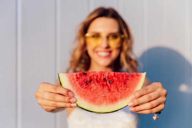 bezauberndes frohes Mädchen, das ein Stück saftige Wassermelone mit Samen hält