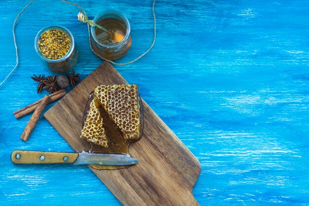 Bienenpollen Glas; Gewürze und Bienenwabenstück mit Messer gegen blauen strukturierten Hintergrund