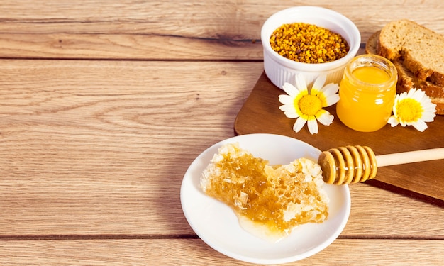 Bienenwabe; Bienenpollen; Honig und Brotscheibe über Holzoberfläche