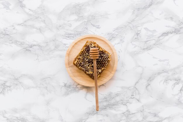 Bienenwabe mit Honigschöpflöffel auf hölzerner Platte