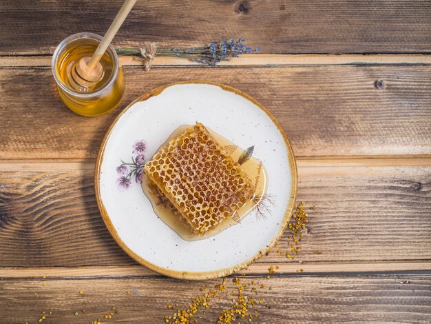 Bienenwabenstück auf weißer Platte mit Honigtopf über dem Holztisch