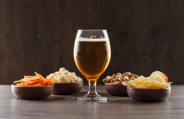 Bier mit Junk Food in einem Becherglas auf Holztisch, Seitenansicht.