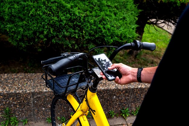 Bike gelb und handy. mann, der einen e-fahrzeugmietservice mit smartphone in der städtischen straße und im park verwendet. junger mann mietet im sommer einen öko-transport.
