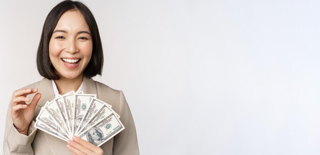 Bild der erfolgreichen Geschäftsfrau, die Geld hält Asiatische Unternehmensfrau mit den Bargelddollarlächeln und -lachen, die über weißem Hintergrund stehen