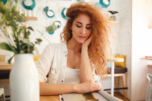 Bild der hübschen schönen rothaarigen jungen Dame, die im Café beim Lesen des Magazins steht. Zur Seite schauen.