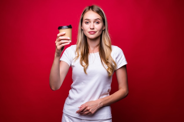 Bild der schönen Frau, die Kaffee zum Mitnehmen in Pappbecher lokalisiert über roter Wand hält