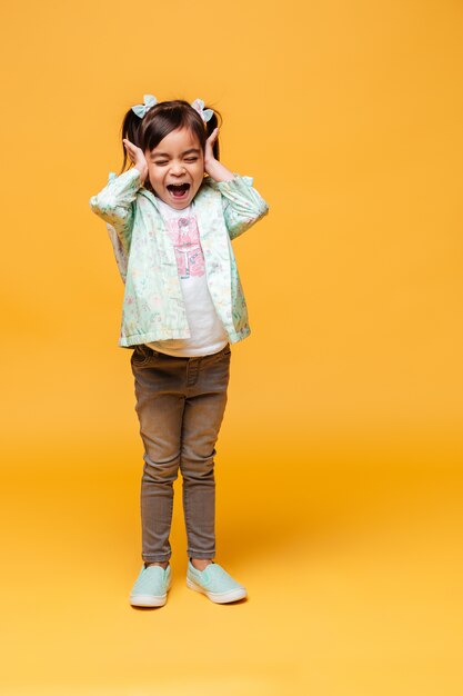 Bild der schreienden emotionalen Kinderstellung des kleinen Mädchens lokalisiert über gelbem Hintergrund.