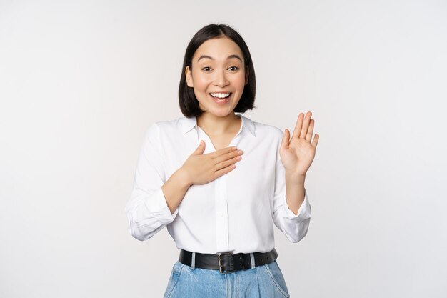 Bild der süßen jungen weiblichen Büroangestellten asiatischen Studentin, die die Hand hochhebt und die Handfläche auf den Brustnamen legt, stellen sich vor und machen das Versprechen, das über weißem Hintergrund steht