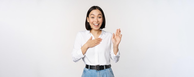 Bild der süßen jungen weiblichen Büroangestellten asiatischen Studentin, die die Hand hochhebt und die Handfläche auf den Brustnamen legt, stellen sich vor und machen das Versprechen, das über weißem Hintergrund steht