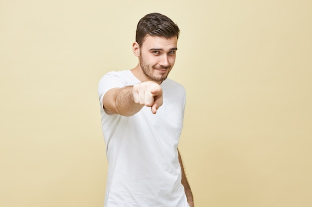 Bild des attraktiven selbstbewussten jungen brünetten Mannes im weißen lässigen T-Shirt, das gerade schaut und Zeigefinger zeigt, Ihnen Vertrauen gibt, brillante Idee habend. Selektiver Fokus