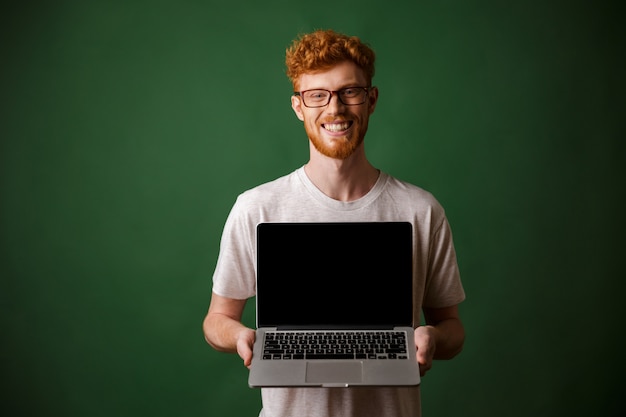 Bild des fröhlichen jungen Lesekopfmannes, der Laptop-Computer hält