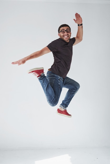 Bild des fröhlichen jungen Mannes, der lässig gekleidet über Weiß springt