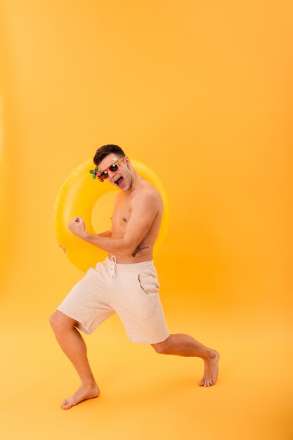 Bild des fröhlichen nackten Mannes in Shorts und Sonnenbrille in voller Länge