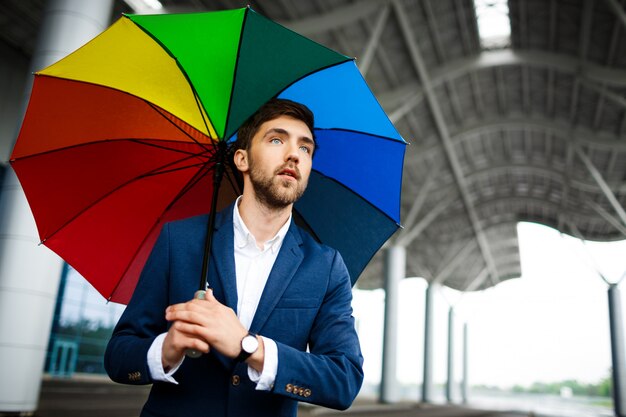 Bild des jungen Geschäftsmannes, der bunten Regenschirm in der Straße hält
