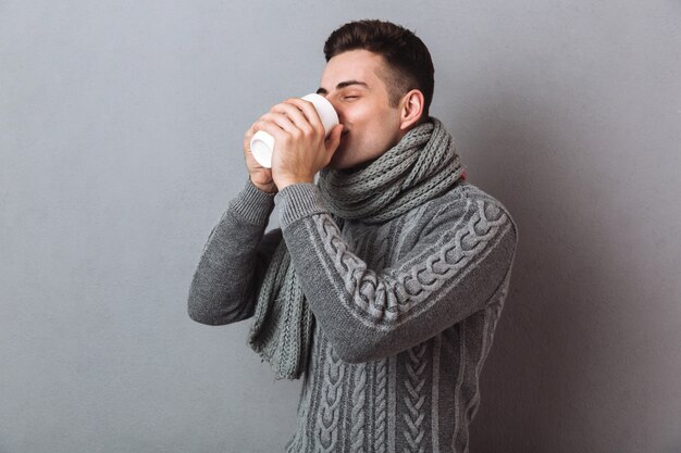 Bild des kranken Mannes in trinkendem Tee der Strickjacke und des Schals