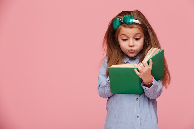 Bild des netten Mädchens mit dem langen kastanienbraunen Haar interessantes Buch lesend, das an der Bildung beteiligt ist