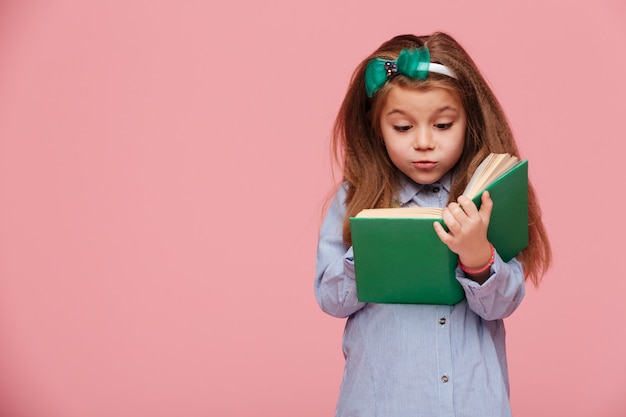 Bild des netten Mädchens mit dem langen kastanienbraunen Haar interessantes Buch lesend, das an der Bildung beteiligt ist