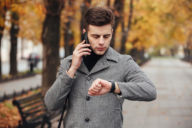 Bild des sachlichen Mannes sprechend am Handy beim Treffen weitergehen, Zeit mit Uhr an Hand überprüfend