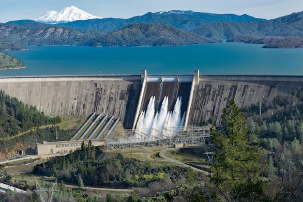 Bild des Shasta-Damms, umgeben von Straßen und Bäumen mit einem See und Bergen