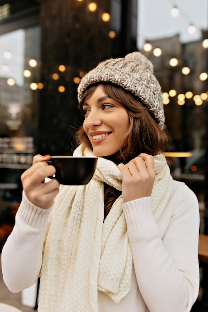 Kostenloses Foto bild des stils der europäischen frau in der strickmütze und im schal, die kaffee trinken und zeit draußen im winter genießen