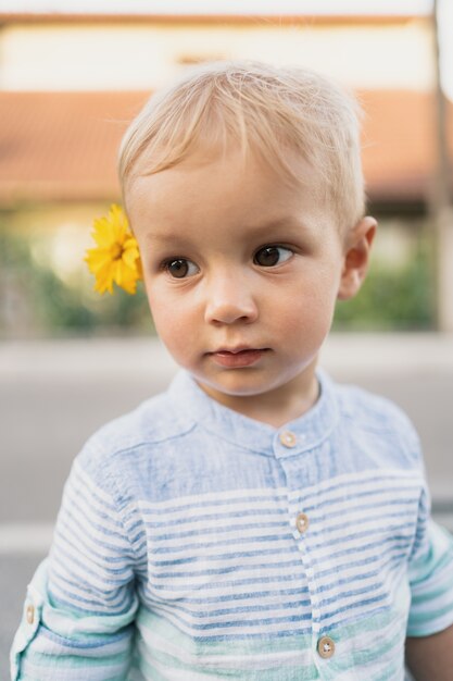 Bild des süßen Jungen, Nahaufnahmeporträt des Kindes mit einer gelben Blume in seinen Haaren