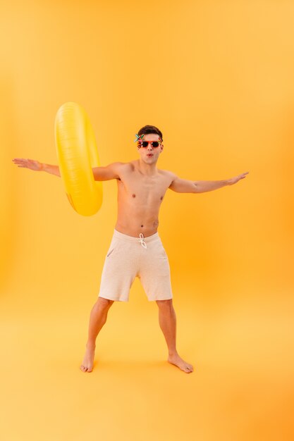 Bild des verspielten nackten Mannes in Shorts und Sonnenbrille in voller Länge