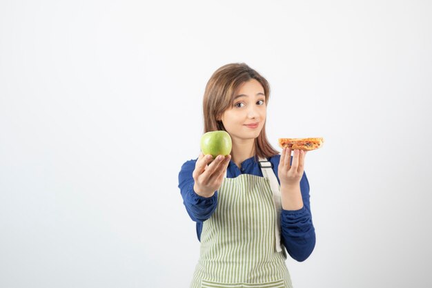 Bild einer Frau in Schürze, die versucht zu wählen, was sie Apfel oder Pizza essen soll?