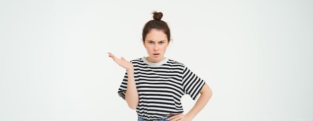 Bild einer frustrierten Frau, die sich beschwert, verwirrt aussieht, mit den Schultern zuckt und die Stirn runzelt und vor Weiß steht