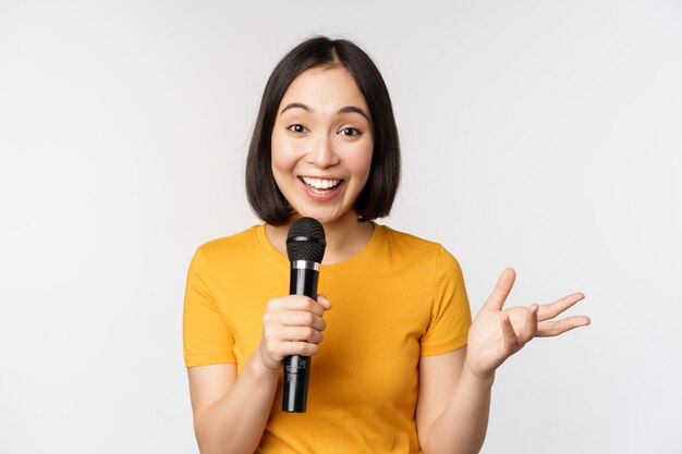 Bild einer jungen asiatischen Frau, die in einer Mikrofon-Performance spricht, wobei das Mikrofon eine Rede hält, die im gelben T-Shirt vor weißem Hintergrund steht