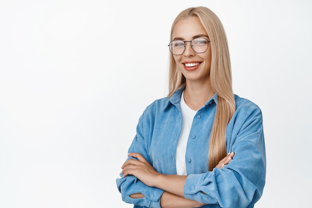 Bild einer jungen blonden Frau mit Brille, die wie ein Profi steht, lächelnd und selbstbewusst mit gekreuzten Armen auf der Brust vor weißem Hintergrund steht