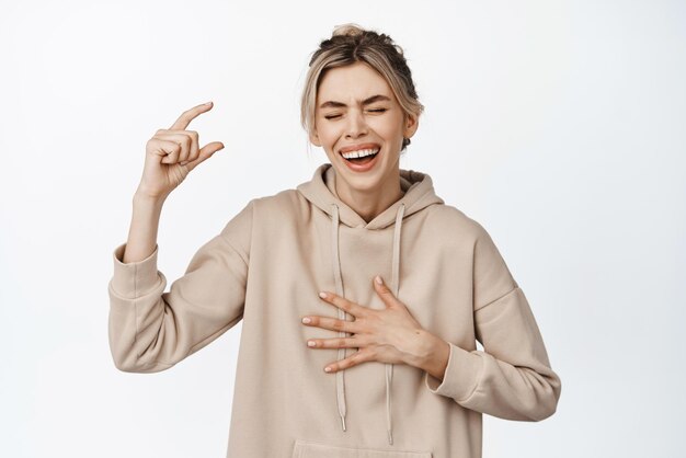 Bild einer jungen Frau, die sich die Finger kneift und etwas Kleines oder Winziges hält, das lachend vor weißem Hintergrund steht