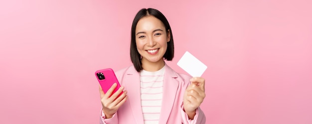 Bild einer lächelnden, glücklichen asiatischen Geschäftsfrau, die eine Kreditkarte zeigt, die online auf Smartphone-Apps bezahlt