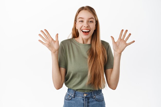 Bild eines aufgeregten und überraschten glücklichen Mädchens, das vor Freude die Hände zittert und fröhlich lacht, im T-Shirt vor weißem Hintergrund steht