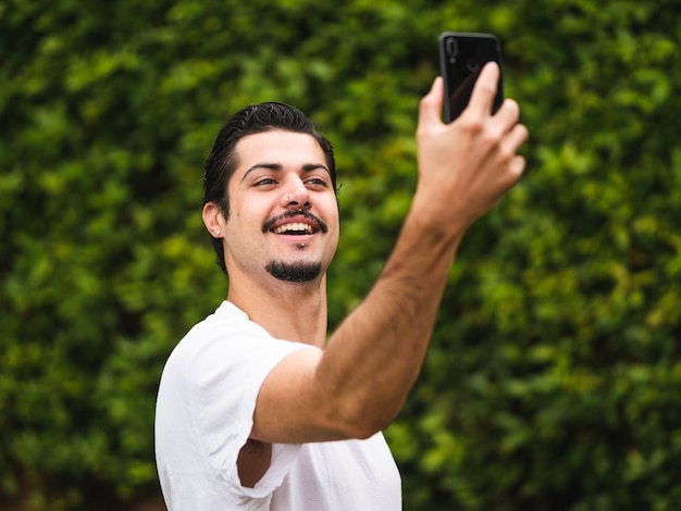 Bild eines brünetten Mannes, der Selfies gegen ein Grün macht