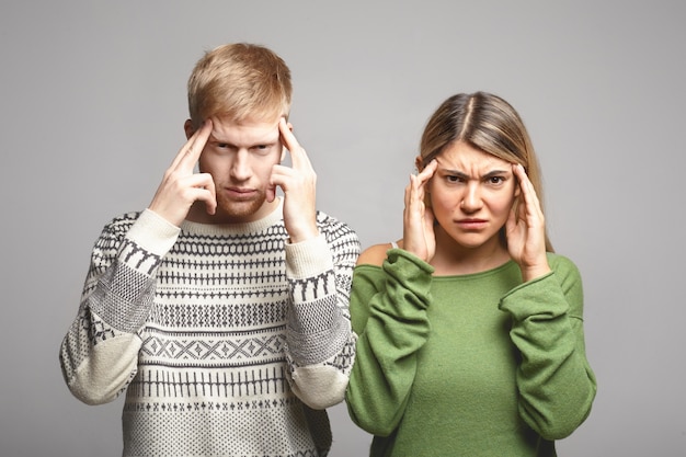 Bild eines ernsthaften konzentrierten jungen Mannes und einer Frau in Freizeitkleidung, die die Stirn runzeln und die Schläfen zusammendrücken, als ob sie versuchen würden, sich an etwas zu erinnern oder schreckliche Kopfschmerzen zu haben. Menschliche Mimik