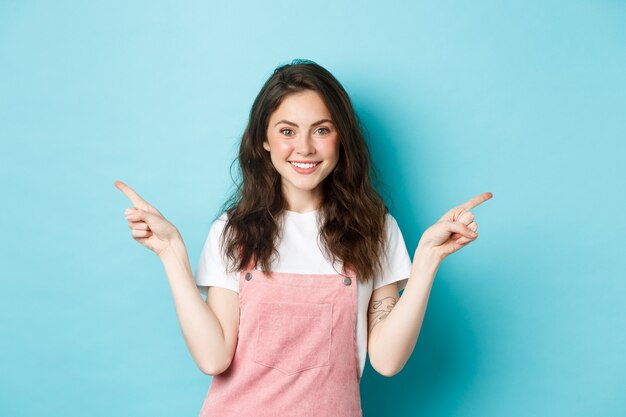 Bild eines glamourösen schönen Mädchens mit hellem Make-up, das mit den Fingern seitlich zeigt und lächelt, zwei Varianten von Promo-Angeboten zeigt, Auswahlmöglichkeiten bietet, blauer Hintergrund.