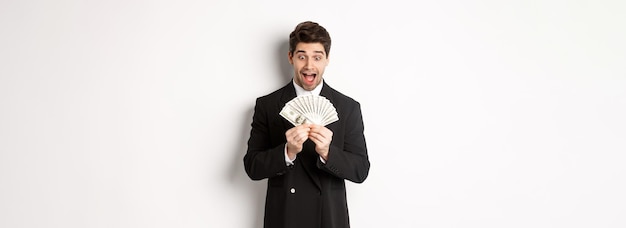 Kostenloses Foto bild eines gutaussehenden bärtigen kerls im schwarzen anzug, der geld mit aufregung betrachtet, der über weißem bac steht
