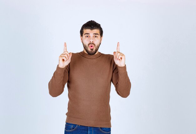 Bild eines jungen attraktiven Modells im braunen Pullover, der Gesten über der weißen Wand macht. Foto in hoher Qualität