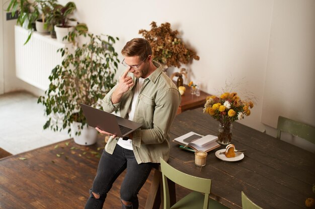 Bild eines jungen erfolgreichen Geschäftsmanns, der auf einem Tisch sitzt und auf einen Laptop schaut, der in einem Büro arbeitet