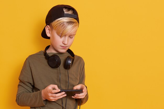 Bild eines Jungen mit Kopfhörern um den Hals, kleiner Kerl, der Wacholdergrünhemd und schwarze hintere Visierkappe trägt