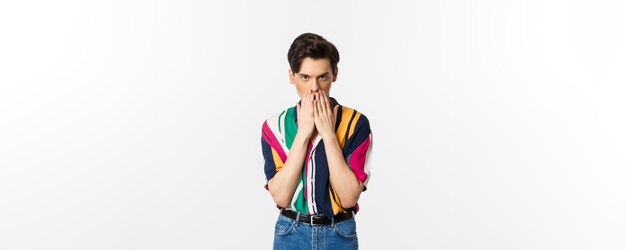 Bild eines jungen schwulen Mannes, der fasziniert aussieht, Händchen auf dem Mund hält und über weißem Hintergrund klatscht
