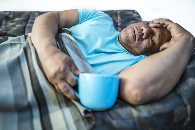 Kostenloses Foto bild eines mannes, der auf einem sofa mit einer blauen tasse liegt