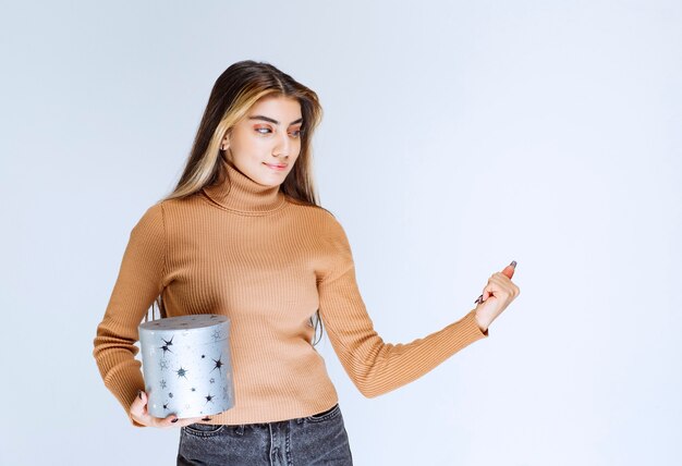 Bild eines Modells der jungen Frau in der braunen Strickjacke, die mit einer Geschenkbox steht und aufwirft.