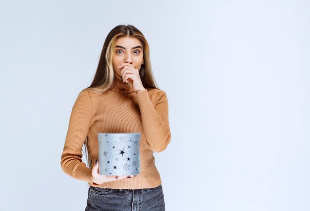 Bild eines Modells der jungen Frau in der braunen Strickjacke, die mit einer Geschenkbox steht und aufwirft.