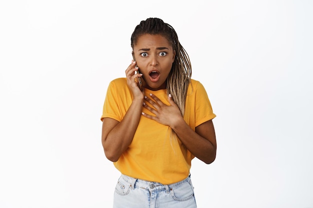 Bild eines schwarzen Mädchens, das einen Anruf entgegennimmt und schockiert auf schlechte Nachrichten reagiert und überwältigt auf den weißen Hintergrund der Kamera starrt