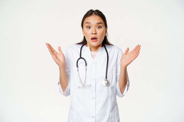 Bild eines überraschten Arztes, der die Hände hebt und schockiert aussieht, während er in der Uniform eines medizinischen Krankenhauses steht ...
