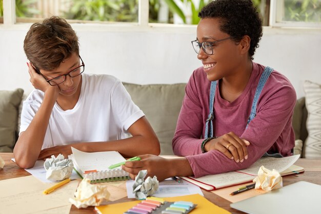 Bild von Jungen und Mädchen gemischter Rassen arbeiten zusammen, um Kursarbeit vorzubereiten, Aufzeichnungen im Notizblock zu machen, auf der Couch zu sitzen, an der Präsentation für die Klasse zu arbeiten, Team zu sein. Lern- und Kollaborationskonzept