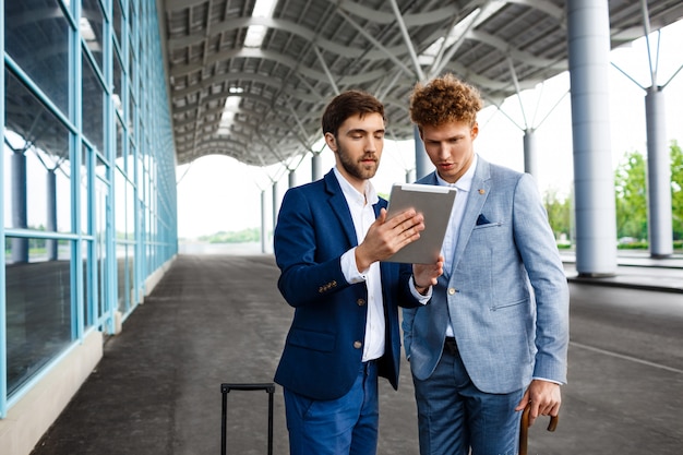 Bild von zwei jungen Geschäftsleuten, die auf Station sprechen und Tablette halten