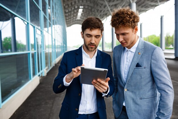 Bild von zwei jungen Geschäftsleuten, die auf Terminal sprechen und Tablette halten