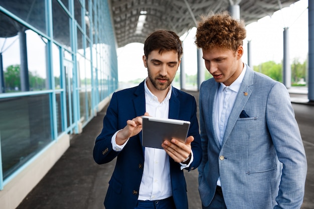 Bild von zwei jungen Geschäftsleuten, die auf Terminal sprechen und Tablette halten